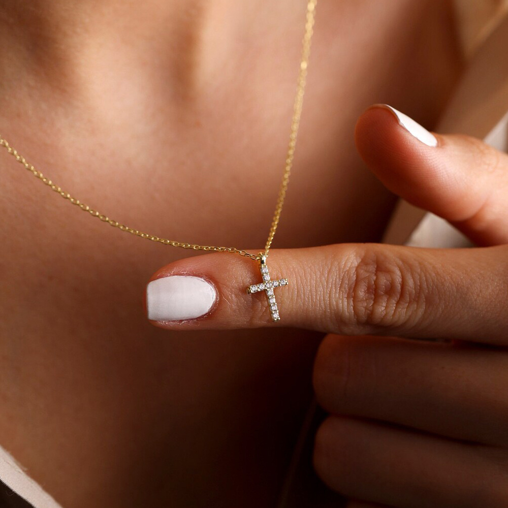 On voit le cou d'une femme qui tient un pendentif croix brillant.