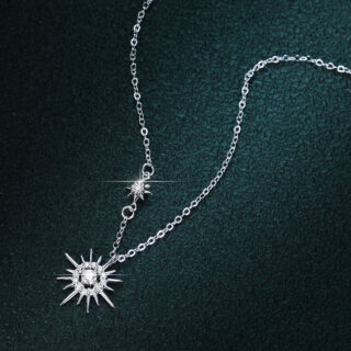 On voit un collier en argent avec un pendentif soleil sur fond noir.