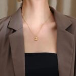 Femme portant un collier avec un petit pendentif doré et un blazer marron avec un tee-shirt noir.