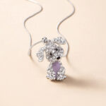 Pendentif représentant un chien brillant avec une pierre violette au centre, fond orangé.