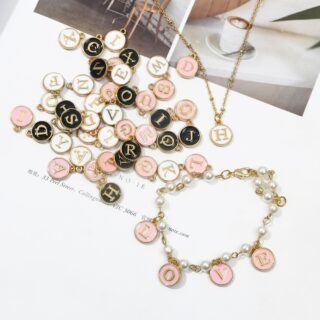 Nombreux pendentifs ronds avec des lettres de l'alphabet de couleur rose, noir et blanc avec des chaines couleur or