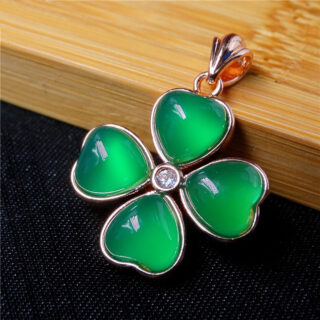 Pendentif trèfle à quatre feuilles de couleur verte sur un fond boisé.