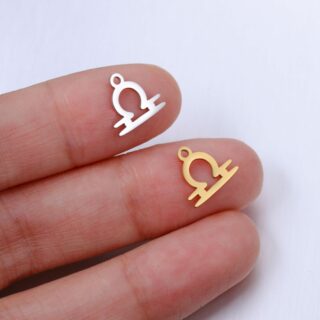 deux pendentifs en forme de signe de la balance, un argenté un doré, sur le bout de deux doigts d'une main blanche, sur fond gris