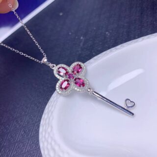 On voit un collier en argent en forme de clé ornée de pierres naturelles roses.