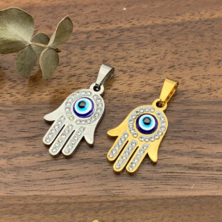 Photo de deux pendentif main de fatma avec un oeil turc au milieu, un argenté et un doré posés sur une table en bois