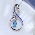 Pendentif argenté avec une topaze bleue en son centre, fond blanc.