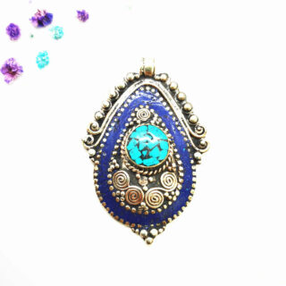 Pendentif tibétain ovale en métal doré avec pierres colorées, couleur bleu sombre aux extrémités, des gravures en forme de spirale au milieu, et une grande pierre turquoise au centre, sur fond blanc