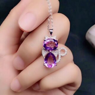 Main de femme tenant un collier avec une chaine et un pendentif en forme de chat e améthyste violette