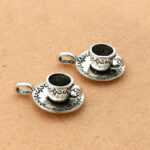 On voit deux pendentifs argentés qui représentent une tasse de thé sur sa soucoupe.