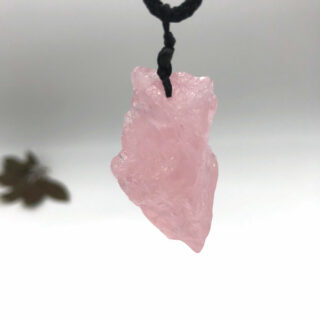 Pendentif pierre brut de quartz rose tenu par un ficelle noire sur fond blanc.