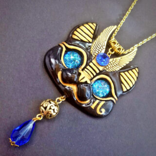 Pendentif en forme de tête de chat egyptienne de couleur dorée, avec des yeux et des perles bleues.
