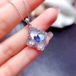 Photo représentant une main montrant un pendentif en argent avec une pierre en saphir au milieu.