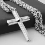 Pendentif crois relief argenté avec sa chaine, posé sur un présentoir noir.