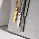 Collier dans 3 coloris différents (or,argent et noir) pour homme avec pendentif rectangulaire en acier, motif chevrons, posé sur une pierre.