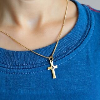 Pendentif en forme de croix dorée avec initiale gravée porté par un enfant qui porte un t-shirt bleu
