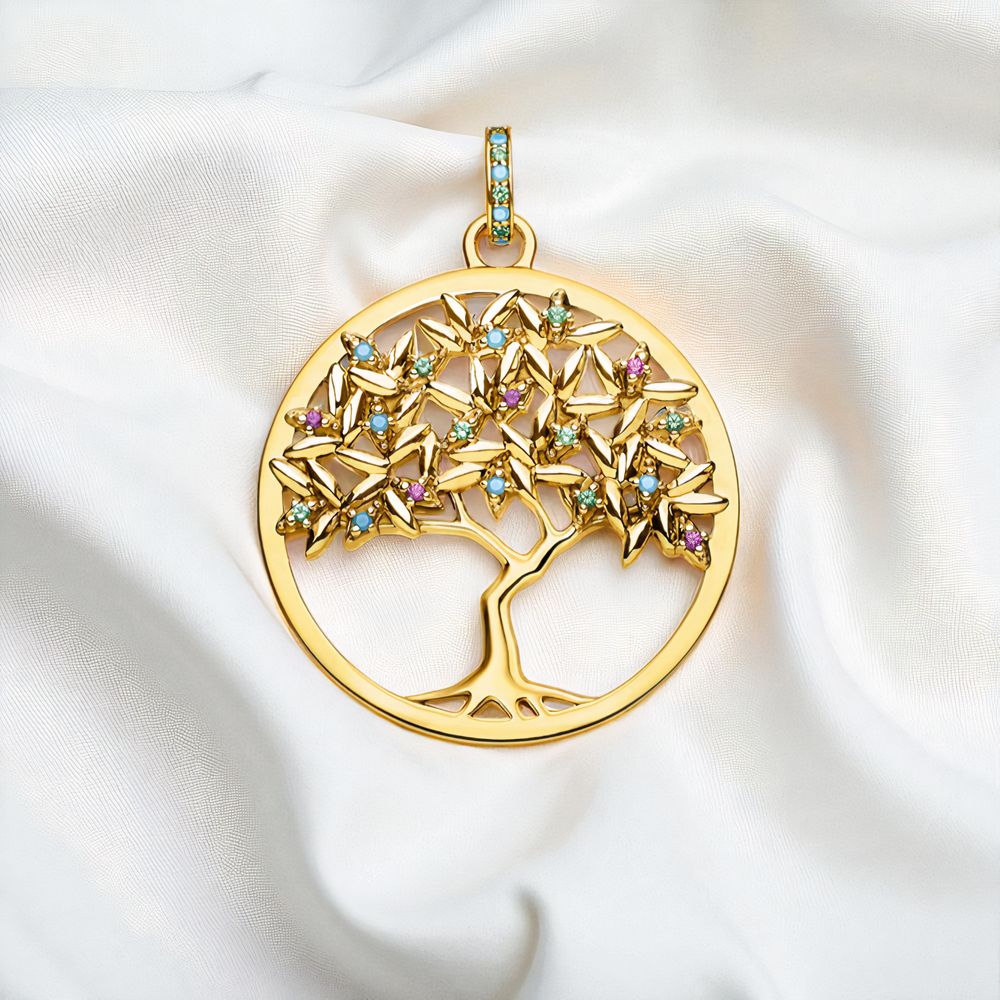 Pendentif rond en plaqué or représentant un arbre de vie ajouré, orné de petits cristaux colorés, sur du tissu blanc