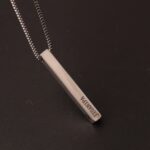 collier en argent avec pendentif en forme de barre rectangulaire fine, avec prénom gravé dessus. Sur fond neutre.