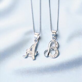 pendentifs lettres en argent en majuscule cursive, ornés de petits zircons, disposés sur fond bleu clair