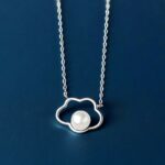 Petit pendentif en forme de nuage creux avec perle ronde au centre, sur chaîne fine en argent, sur fond neutre bleu foncé