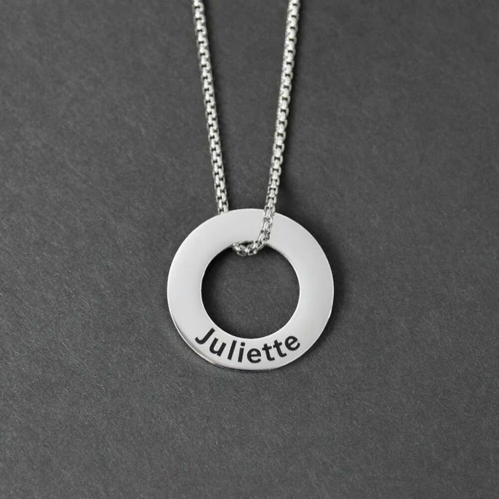 Pendentif en forme d’anneau argenté gravé du prénom Juliette, monté sur une chaîne en acier. Sur fond neutre.
