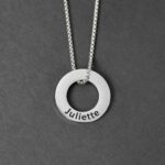 Pendentif en forme d’anneau argenté gravé du prénom Juliette, monté sur une chaîne en acier. Sur fond neutre.