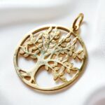Pendentif rond doré représentant un arbre de vie finement travaillé, posé sur du tissu blanc.
