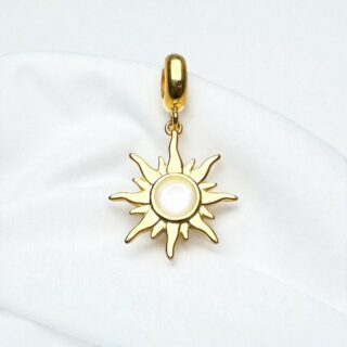 Pendentif doré en forme de soleil avec centre en nacre blanche, posé sur du tissu blanc