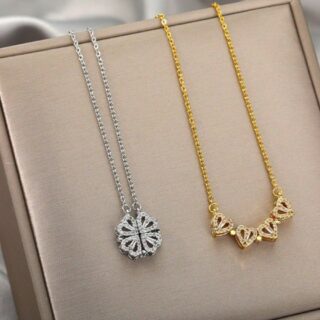 Pendentif en forme de trèfle à quatre feuilles argenté à coté d'un collier doré où le trèfle est ouvert formant 4 coeurs, décoré de strass, sur un présentoirà bijoux.